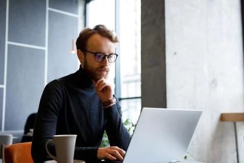 A young red-haired guy, a programmer or entrepreneur in glasses, works in a Stock Photos