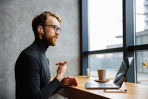 A young red-haired guy, a programmer or businessman in glasses, is sitting in a Stock Photos