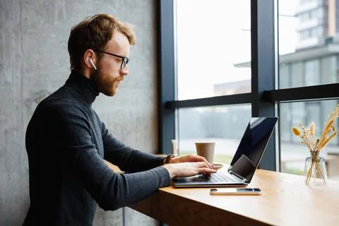 A young red-haired guy, a programmer or entrepreneur in glasses, works in a Stock Photos