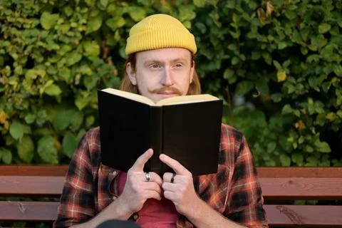 A young red-haired guy sits on a park bench and watches those around Stock-Fotos