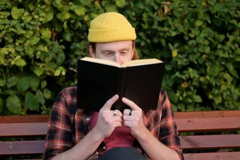 A young red-haired guy sits on a park bench and watches those around Stock Photos