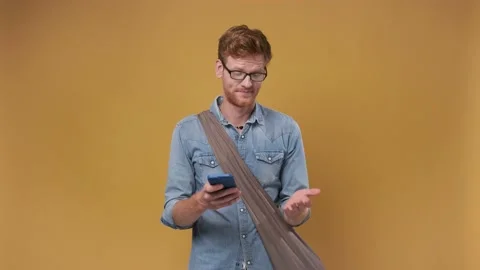 Young red-haired handsome man looks at smartphone in bewilderment, dissatisfied Stock Footage 239653608