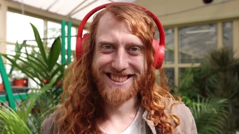 A young red-haired man listens to music in winter garden, filled with plants. Stock Footage 252736337