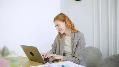 Young red-haired mother working on laptop at stylish desk with stationery in a Stock Footage 308491327