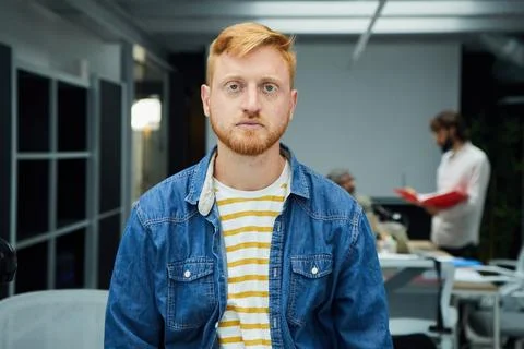 Young red-haired programmer or businessman in modern office looking seriously at Stock-Fotos