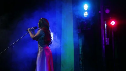A young red-haired singer sings on stage with professional lighting and puffs of 스톡 동영상 105965691