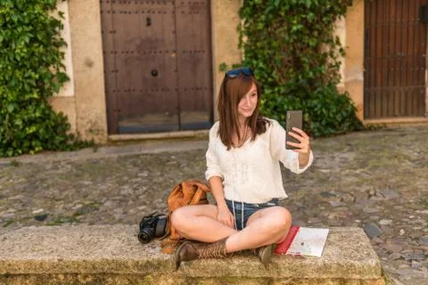 A young red-haired tourist with backpack, camera and city map takes a selfie in Stock Photos
