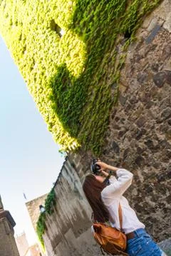 A young red-haired tourist takes a photograph of a tower covered in green ivy in Stock Photos