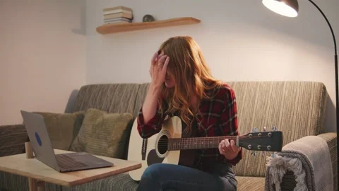 Young red-haired woman learning accords playing acoustic guitar while sitting on Stock Footage 316762489
