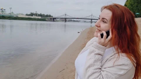 Young red-haired woman talking on phone and laughing. Lady uses modern smartp Stock Footage 211889641