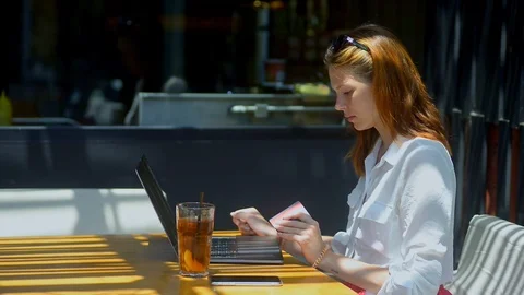 Young red haired woman using laptop and card sitting in summer cafe while 스톡 동영상 123090601