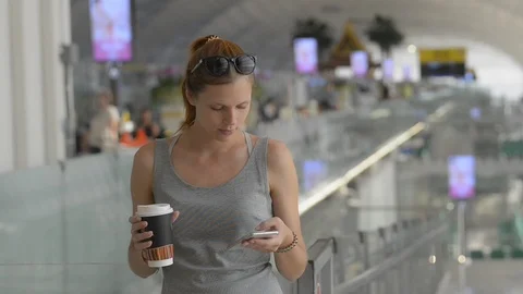 Young red haired woman using smartphone and holding coffee in hand standing in Stock Footage 123091837