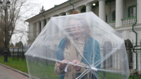 Young red-haired woman in a white coat and a blue scarf walks against the Video stock 159190879