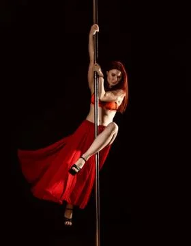 Young redhead athletic pole dance girl in a red dress on a black studio Stockfoto's