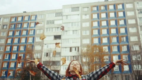 Young redhead girl throws bunch of autumn leaves over her head near the building Stockbeeldmateriaal 218319634