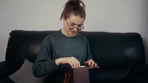 The young redhead, with glasses, opens the gift and is surprised by what she Stock-Footage 160479680