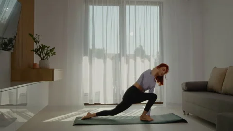 Young redhead practices yoga in bright living room at sunrise Stock Footage 309327545
