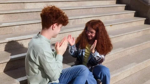 Young redhead siblings playing hand game on outdoor staircase in sunlight Stock Footage 320768637