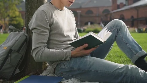 Young relaxed guy is reading modern fiction sitting on the plaid mear college. Stock Footage 101795267