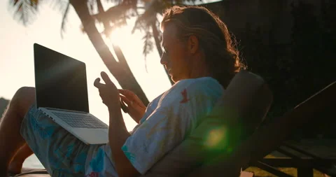 A young relaxed man working on the beach using a smartphone and laptop Stock Footage 105727938
