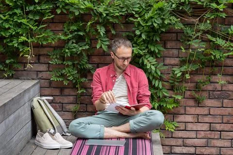 Young relaxed student guy sitting in lotus pose reading book outdoors, enjoying 스톡 사진