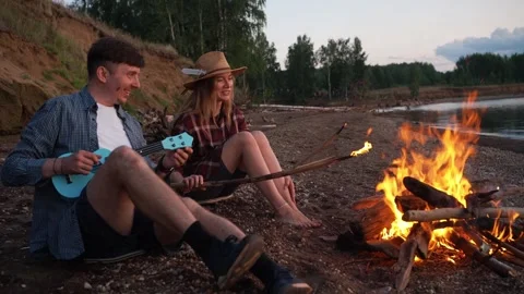 Young romantic couple enjoying a date on a riverbank, with the man playing a Stock Footage 345961175