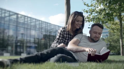 Young romantic couple lying in park and reading book. 스톡 동영상 54676178