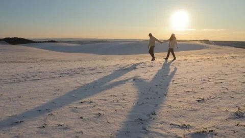 Young romantic couple walks casting long shadows on snow at winter sunset Video stock 327870624