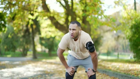 A young runner has shortness of breath during a morning run in a city park. Stock Footage 234876634