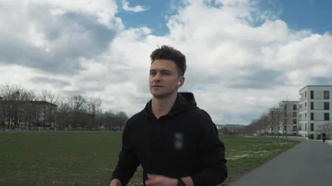 Young runner jogging in an urban city park. A man listens to music in headphones Stock Footage 271742085