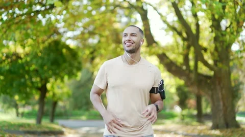 The young runner of mixed race with headphones and a smartphone jogging in an  Stock Footage 234870772