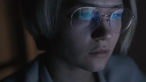Young sad woman in glasses flips news feed in computer in dark room Stock Footage