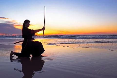 Young samurai women with japanese sword(katana) at sunset on the beach Stock Photos
