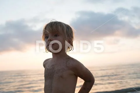 Young sand dirty child girl serious portrait beach shore. Warm sunset light Stock Photos