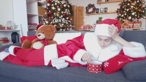 Young Santa Claus eats Christmas gingerbread with raisins lying on the sofa Stock Footage 165462733