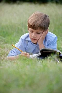 Young school boy doing homework alone, lying on grass Stock Photos