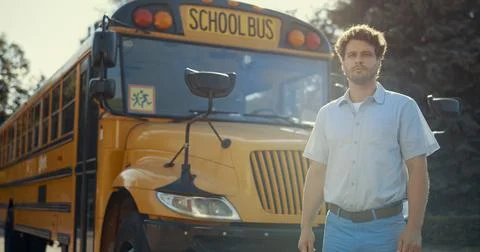 Young schoolbus driver stand near academic shuttle alone. Chauffeur man posing. Stock Photos