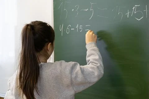 A young schoolchild solves a complex math problem on a green chalkboard in .. Stock Photos