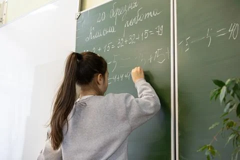 A young schoolchild writes complex math equations with white chalk on a gre.. Stock Photos