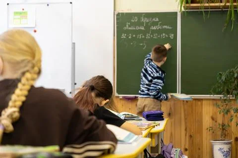 A young schoolchild writes complex math equations on a green chalkboard in .. Stock Photos