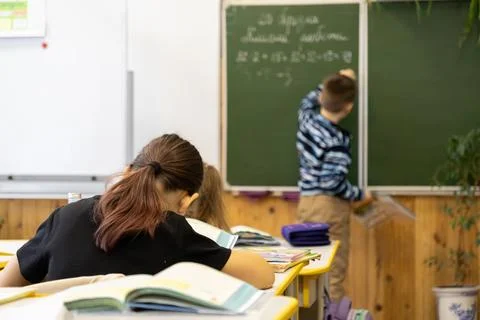 A young schoolchild writes math problems on a bright green chalkboard in an.. Stock Photos