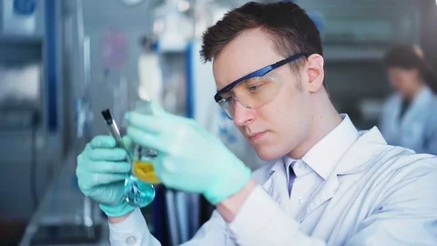 Young scientist checking test tubes in the lab. Man wears protective goggles Stock Footage 85327957