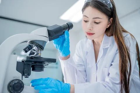 Young scientist examines sample under microscope in a modern laboratory setti Stock Photos