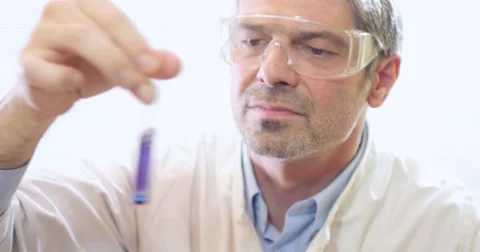 A young scientist holding and examining a test tube with a purple-blue content Stock Footage 48976998