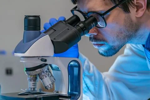 Young scientist in laboratory is looking inside microscope. Stock Photos