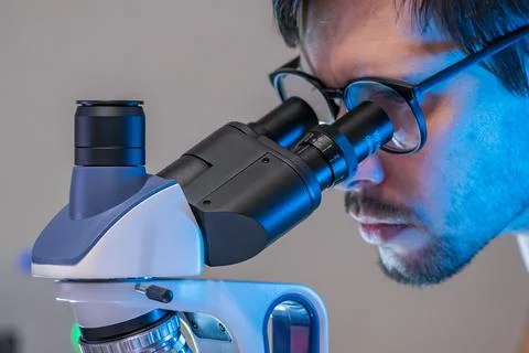 Young scientist in laboratory is looking inside microscope. Microbiology conc Stock Photos