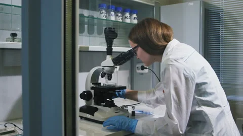 Young scientist looks attentively in microscope at examination Stock Footage 94564029