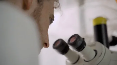 Young scientist removes his protective glasses and looks inside a microscope Stock Footage 112596116
