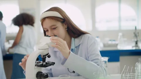 Young scientist smiles while examining samples through microscope Stock Footage 340448711