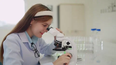 Young scientist smiles while examining samples through microscope Stock Footage 340448722
